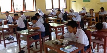 Para siswa SMPN 16 Ambon tampak menikmati program makan bergizi gratis di dalam ruangan kelas, Selasa (22/1/2024). (Foto: Husen Toisuta/Ambonkita.com)